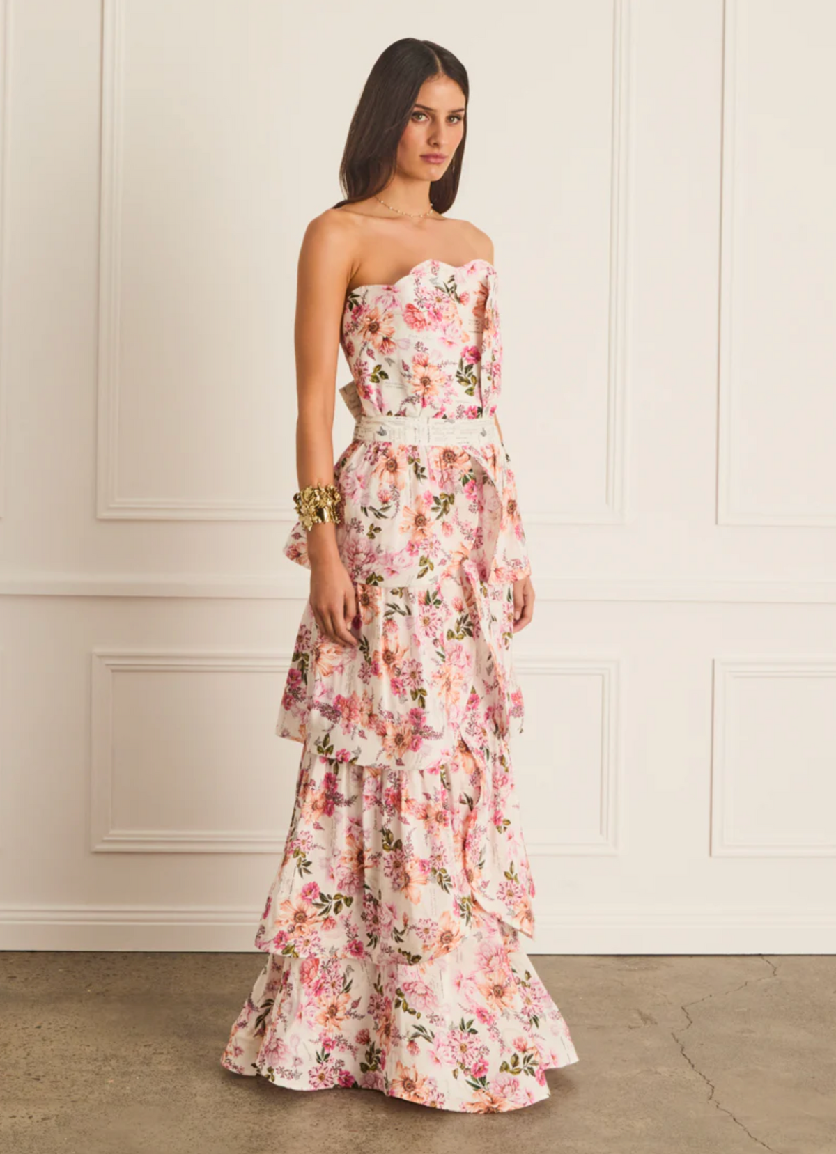 Woman wearing a floral strapless dress against a white wall.